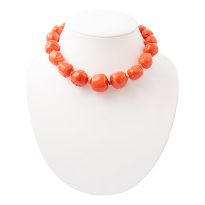 A chunky coral-orange beaded necklace displayed on a white jewelry bust against a white background.