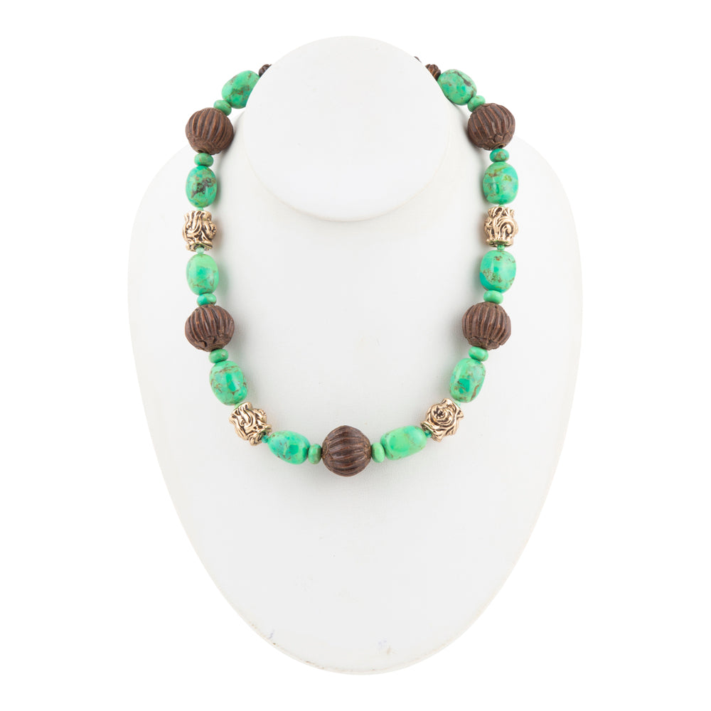 A beaded necklace displayed on a white mannequin bust, featuring green and brown beads with textured metallic gold accents.