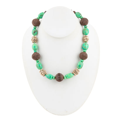 A beaded necklace displayed on a white mannequin bust, featuring green and brown beads with textured metallic gold accents.