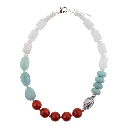 A beaded necklace featuring white translucent rectangular beads, light blue oval beads, faceted red round beads, and a textured silver filigree accent bead, displayed on a clean white background.