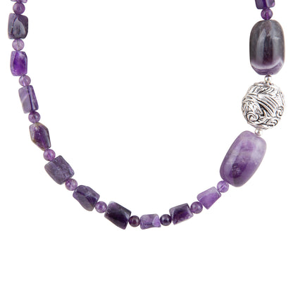 A beaded necklace featuring natural purple amethyst stones in various shapes, including rectangular chips and small round beads, accented by a textured silver spacer bead, shown on a plain white background.