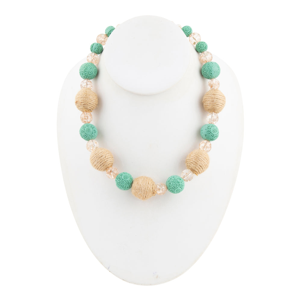A beaded necklace displayed on a white jewelry bust, featuring textured mint green beads, natural tan woven beads, and clear faceted crystal beads.