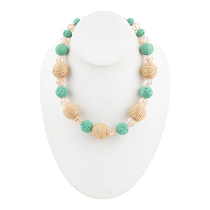 A beaded necklace displayed on a white jewelry bust, featuring textured mint green beads, natural tan woven beads, and clear faceted crystal beads.