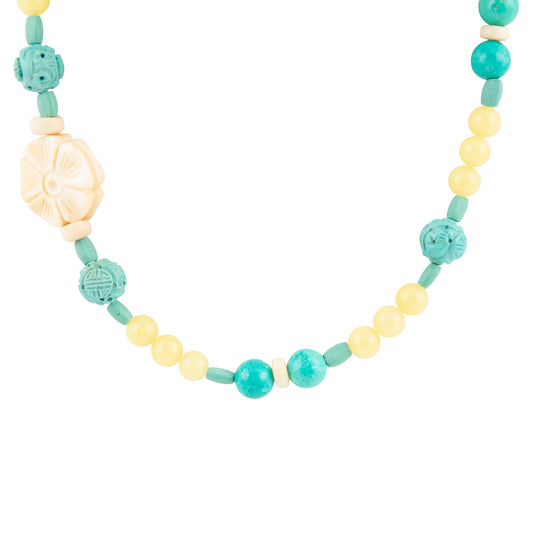 A beaded necklace featuring light yellow round beads, turquoise carved round beads, and a large cream-colored carved flower bead, displayed on a solid white background.