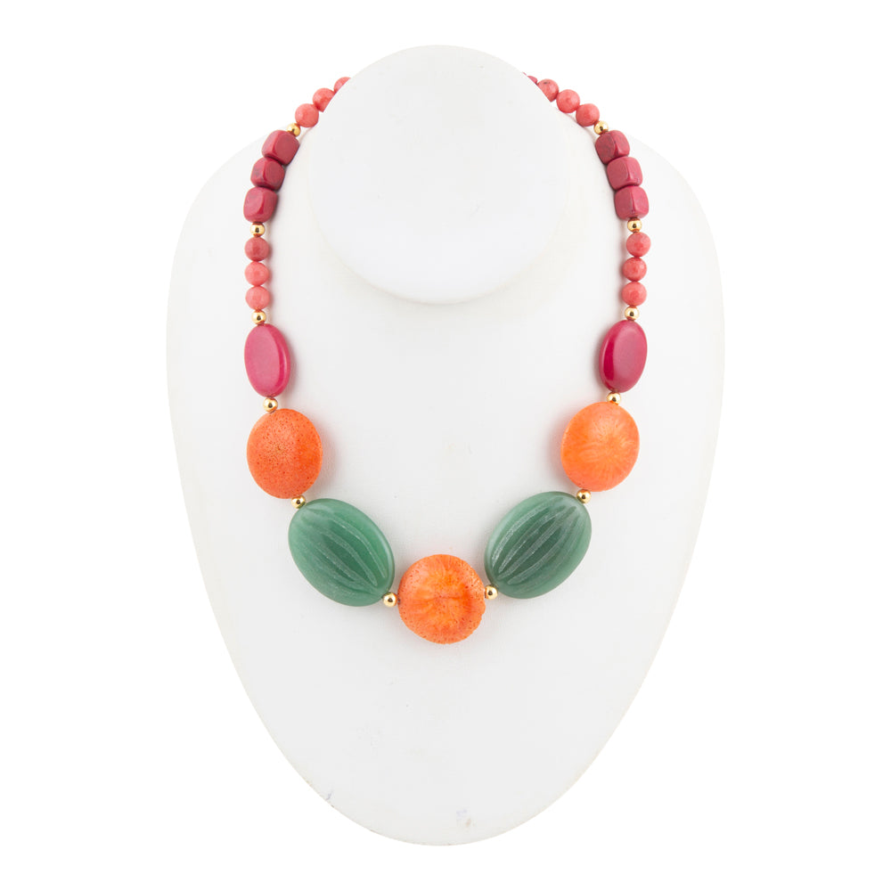 A multi-colored beaded necklace displayed on a white mannequin bust. The necklace features a strand of small pinkish-red beads, oval magenta beads, orange round beads, and two larger textured green oval beads, separated by small gold spacers.