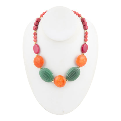 A multi-colored beaded necklace displayed on a white mannequin bust. The necklace features a strand of small pinkish-red beads, oval magenta beads, orange round beads, and two larger textured green oval beads, separated by small gold spacers.