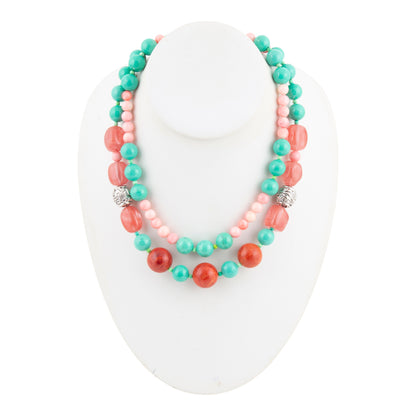 A double-strand beaded necklace displayed on a white mannequin bust. The necklace features turquoise beads, coral-red beads, and light pink beads, accented with two silver-toned spacer beads.