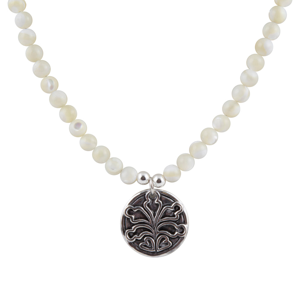 A beaded necklace featuring round, lustrous white pearl-like beads and a circular silver pendant with an engraved floral or leaf motif, shown on a plain white background.