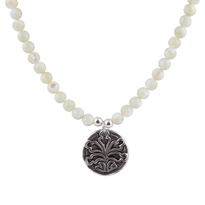 A beaded necklace featuring round, lustrous white pearl-like beads and a circular silver pendant with an engraved floral or leaf motif, shown on a plain white background.