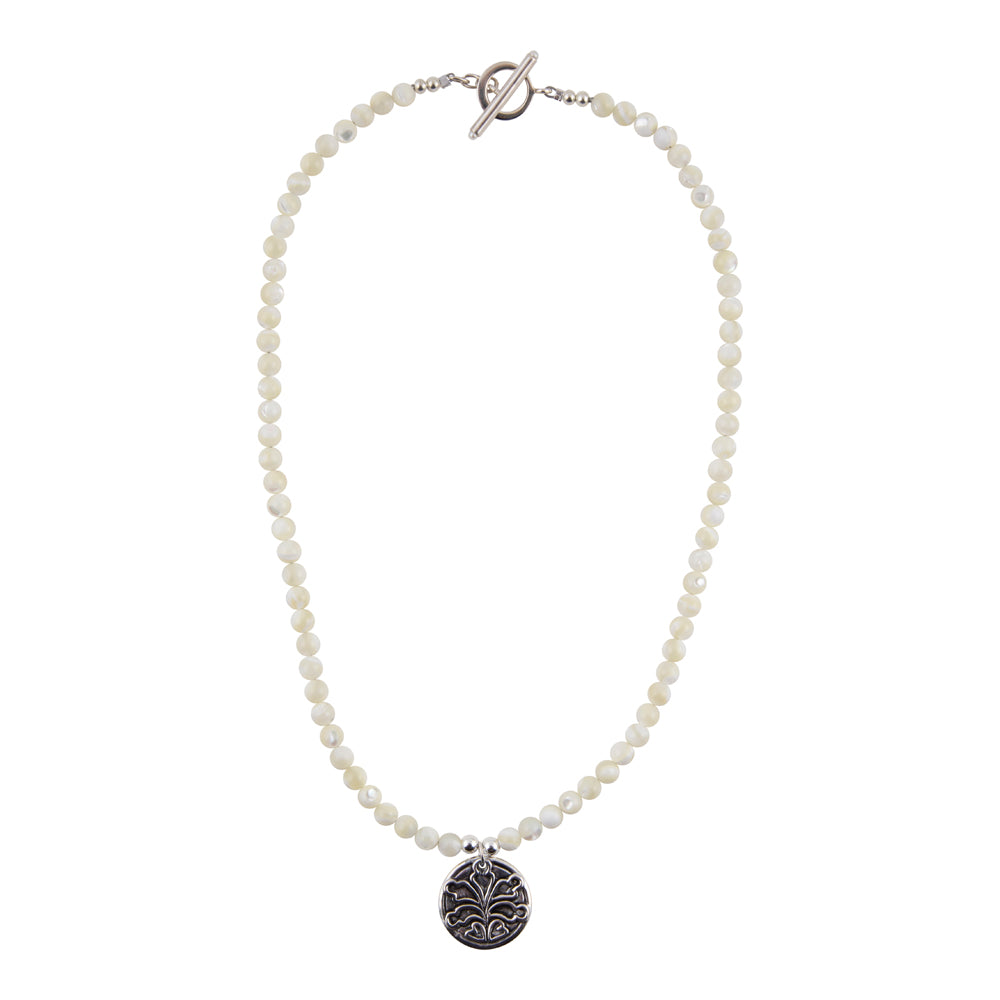 A beaded necklace featuring small, round off-white beads and a silver-toned toggle clasp, with a circular silver pendant engraved with a floral pattern, shown against a plain white background.