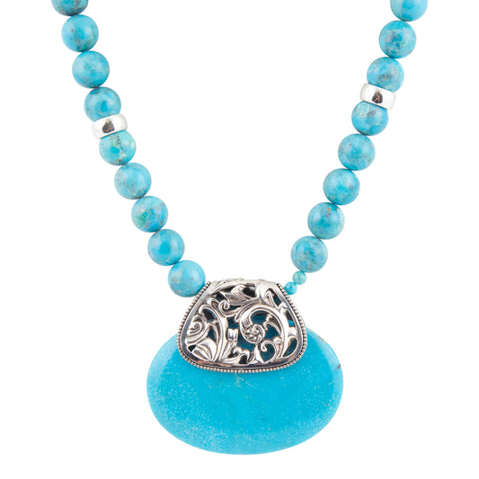 A turquoise beaded necklace with a large turquoise stone pendant, featuring a silver filigree heart-shaped ornament and small silver spacer beads, set against a plain white background.