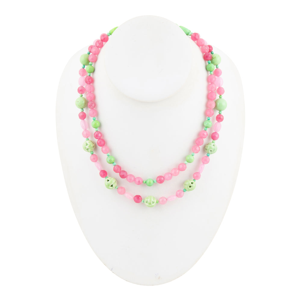 A double-strand beaded necklace displayed on a white mannequin bust. The necklace features alternating pink and light green beads, with some light green beads decorated with small white smiley faces.