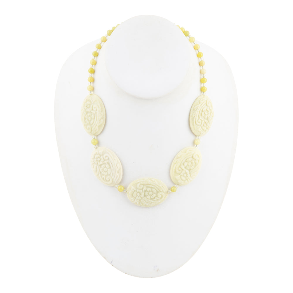 A beaded necklace with five carved oval beads and small yellow beads, displayed on a white mannequin bust against a white background.