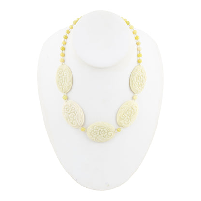 A beaded necklace with five carved oval beads and small yellow beads, displayed on a white mannequin bust against a white background.