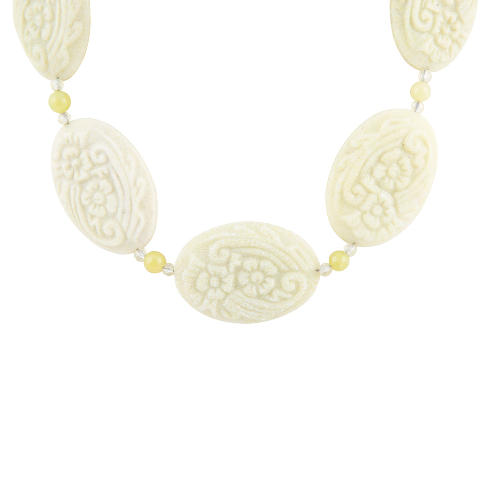 A necklace featuring five carved oval beads in an ivory/cream tone with floral and scroll patterns, separated by small pale yellow beads on a white background.
