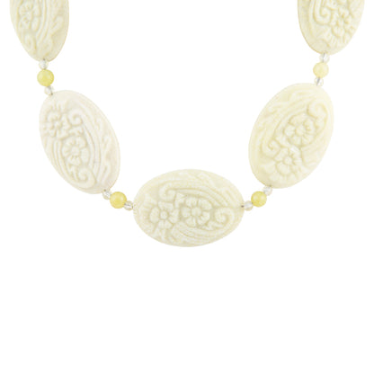 A necklace featuring five carved oval beads in an ivory/cream tone with floral and scroll patterns, separated by small pale yellow beads on a white background.