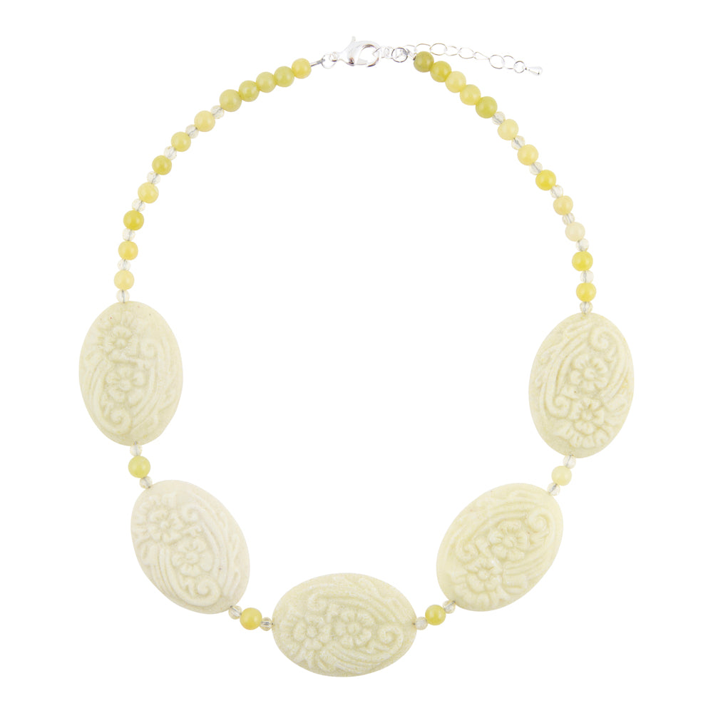A beaded necklace featuring five large, oval, cream-colored carved beads separated by small, light yellow beads, with a silver clasp and extender chain.