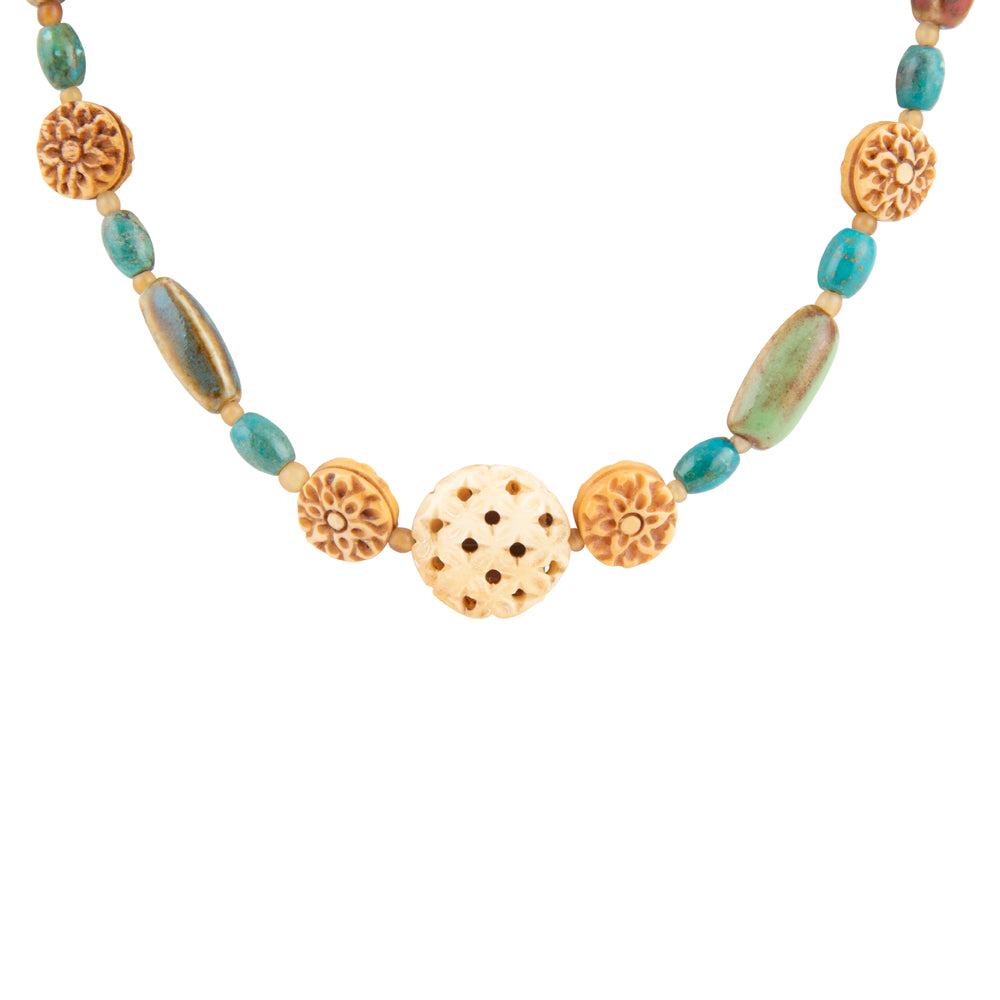 A beaded necklace featuring turquoise-blue oval beads, carved tan floral disc beads, and a central natural ivory bone bead with perforations, displayed on a clean white background.