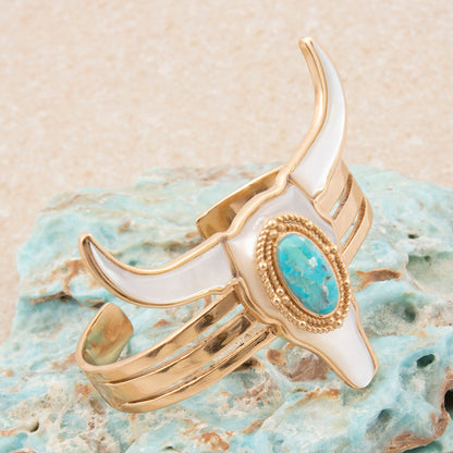 Gold and white horn-shaped ring with turquoise stone on a textured surface