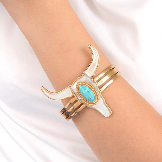 Gold and white bull head bracelet with turquoise stone on a wrist against a white background