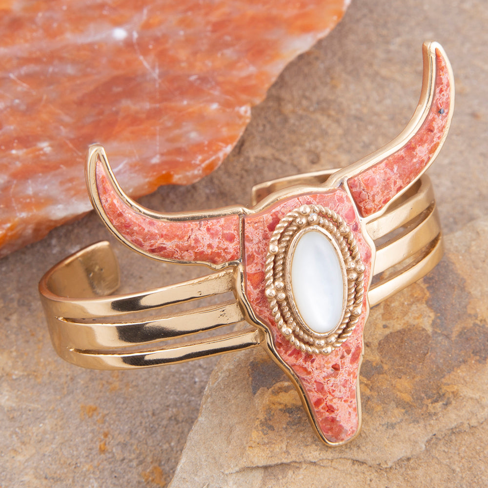 Gold and pink stone bracelet with a central stone on a stone surface