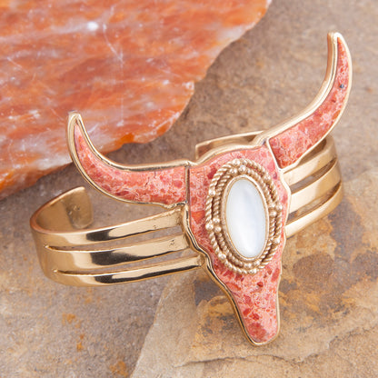 Gold and pink stone bracelet with a central stone on a stone surface