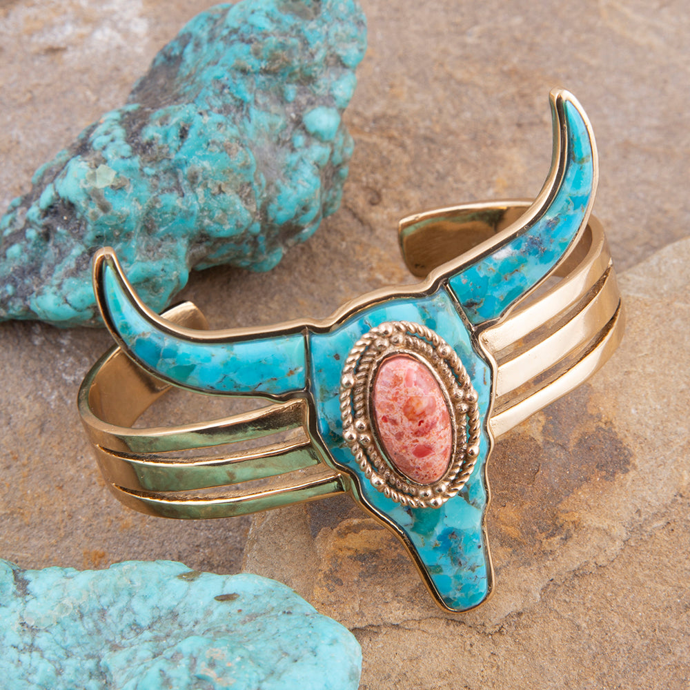 Turquoise and gold horn-shaped bracelet with a pink stone on a stone background
