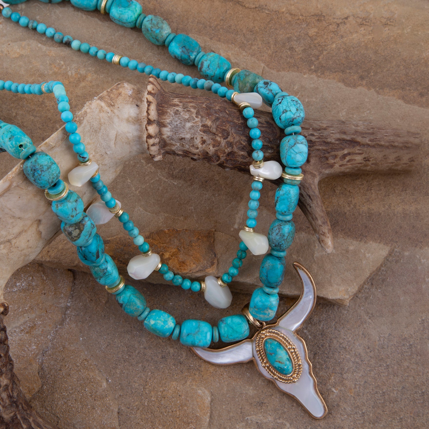 Turquoise beaded necklace with a white shell pendant on a stone surface