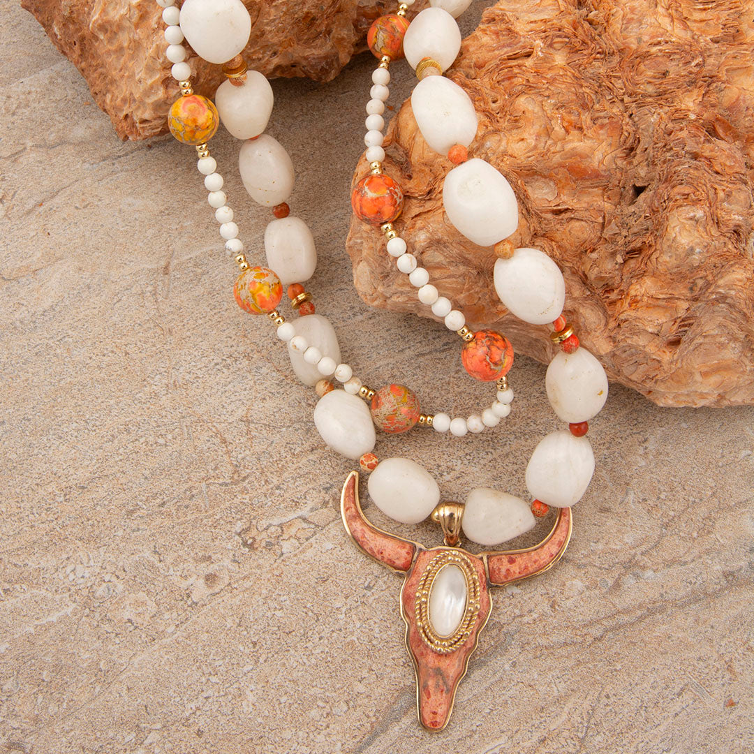 Necklace with white and orange beads and a decorative clasp on a stone surface