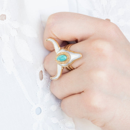 Hand wearing a gold ring with a turquoise stone on a light background