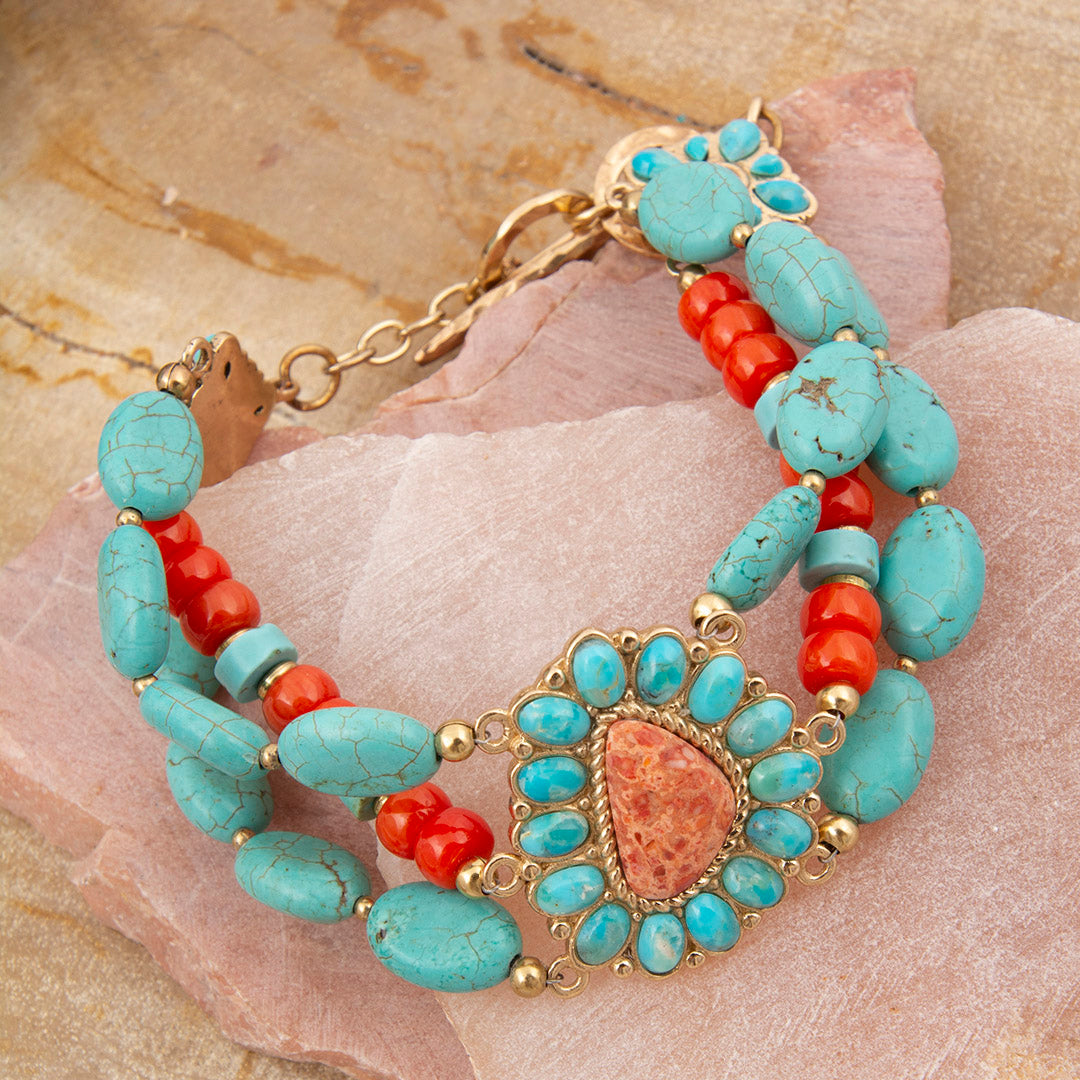 Turquoise and red beaded bracelet with gold accents on a stone surface