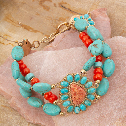 Turquoise and red beaded bracelet with gold accents on a stone surface
