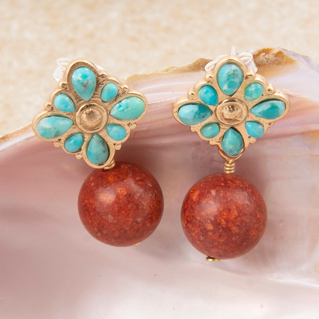 Pair of earrings with turquoise floral design and red stone beads on a shell background