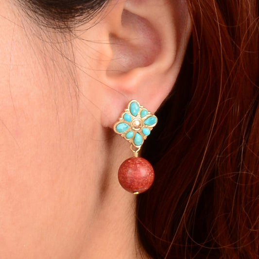 Earring with turquoise flower design and red bead worn by a person