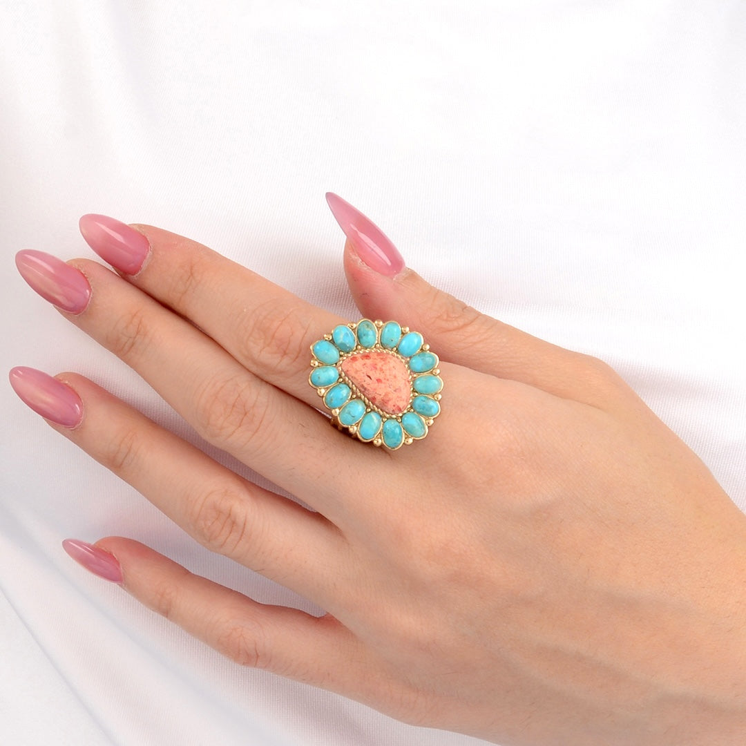 Hand wearing a ring with a pink stone and turquoise accents on a white background