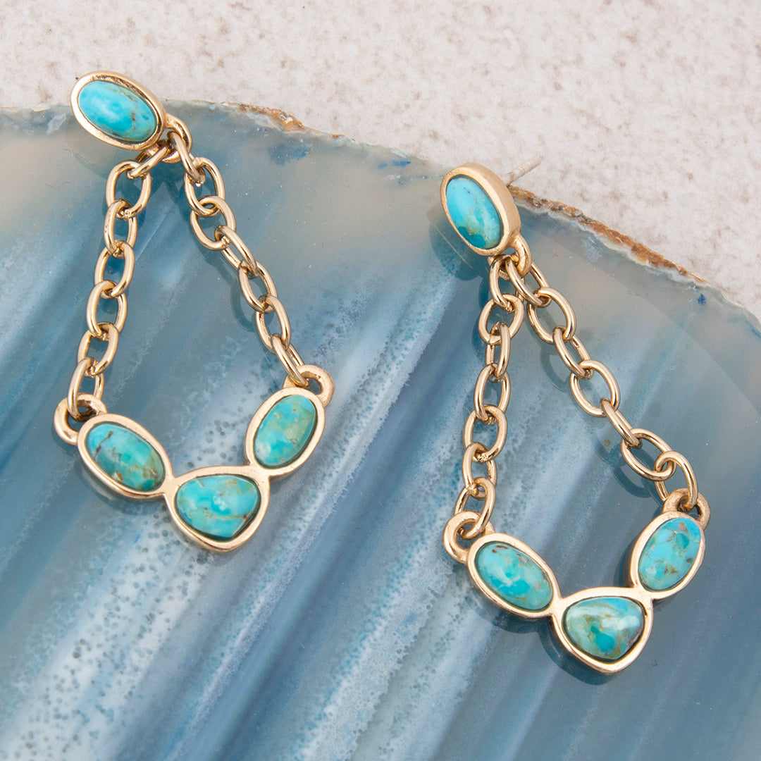 Gold chain earrings with turquoise stones on a textured blue surface