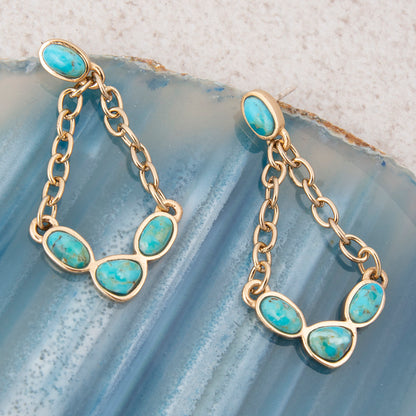 Gold chain earrings with turquoise stones on a textured blue surface