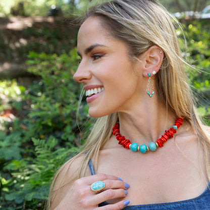 Woman wearing a red and turquoise beaded necklace with matching earrings outdoors.