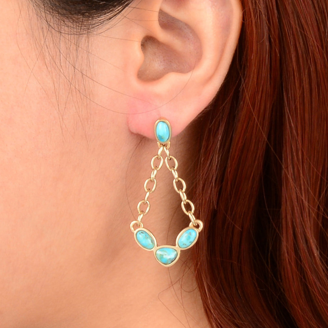 Close-up of an ear wearing a turquoise earring with gold chain