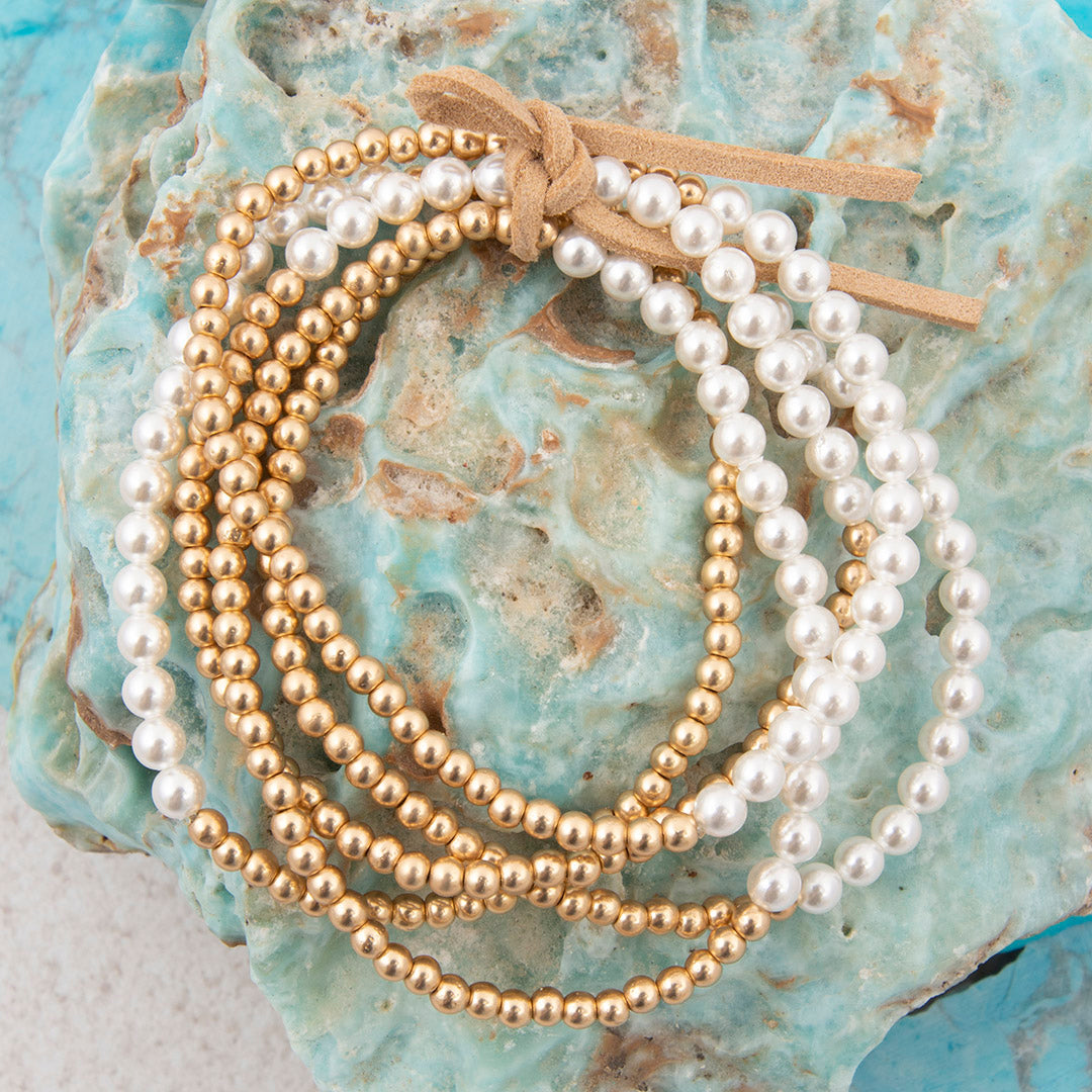 Gold and white beaded bracelets on a textured blue surface