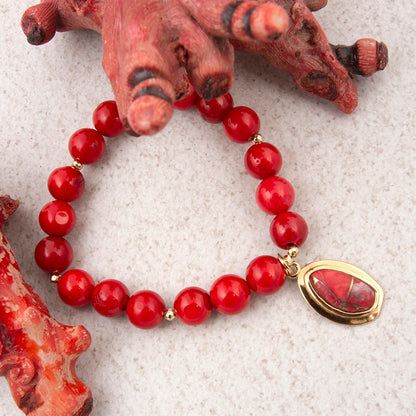 Red beaded bracelet with a gold pendant on a textured surface