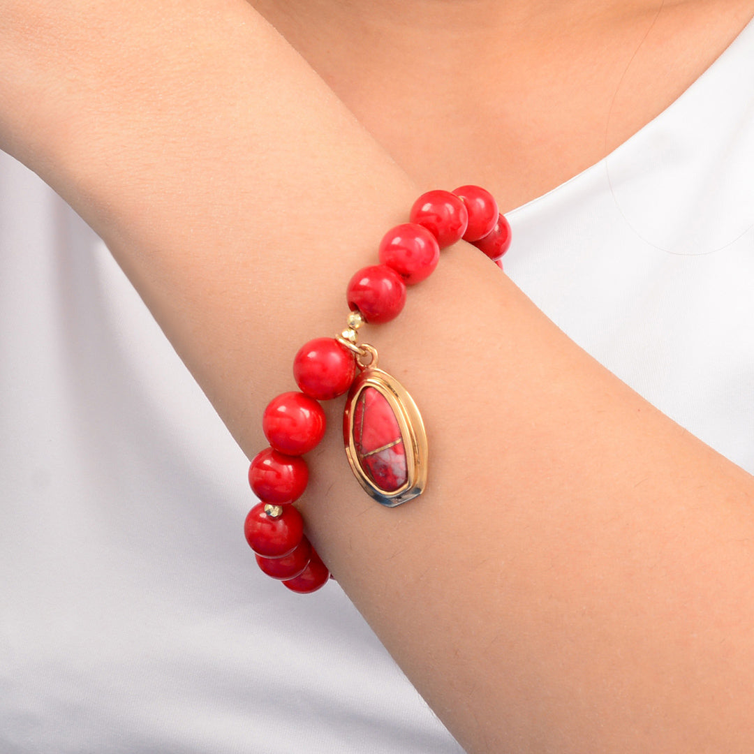Red beaded bracelet with a gold charm on a wrist against a white background