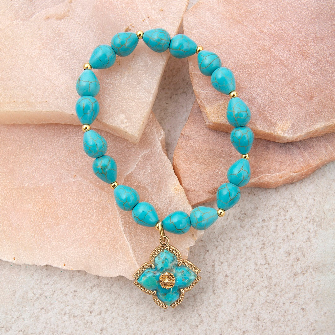 Turquoise beaded bracelet with a gold flower charm on a stone background