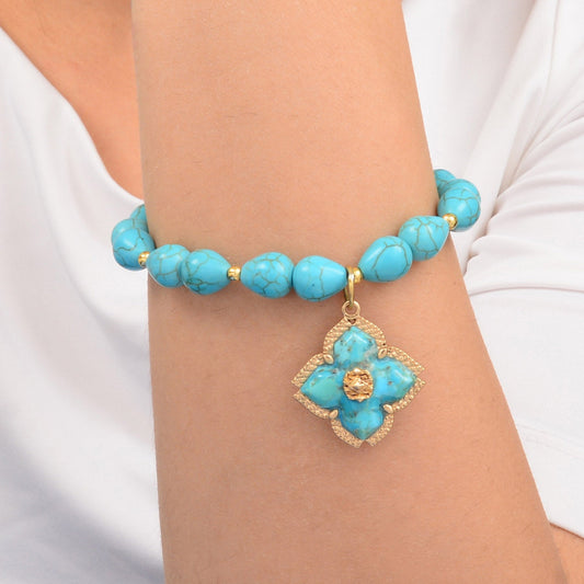 Turquoise beaded bracelet with a gold flower charm on a wrist against a white background