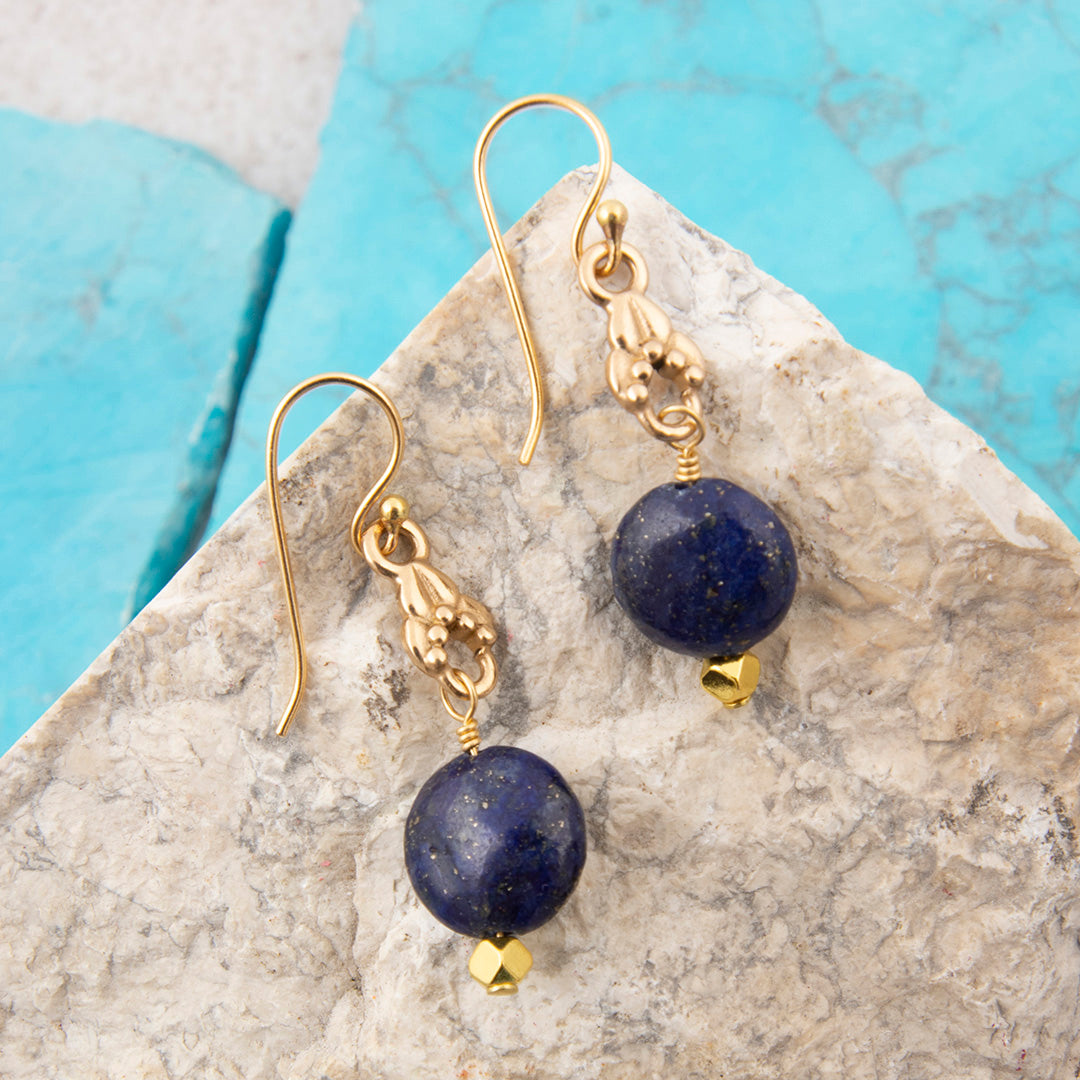 Gold earrings with blue beads on a stone surface
