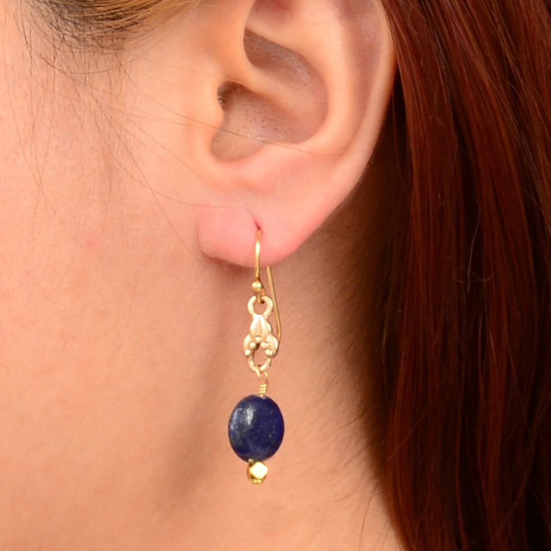 Gold earring with a blue gemstone worn by a person with red hair.