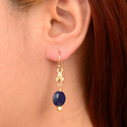 Gold earring with a blue gemstone worn by a person with red hair.