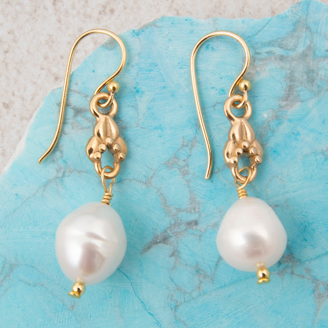 Gold earrings with white pearls on a blue marble surface