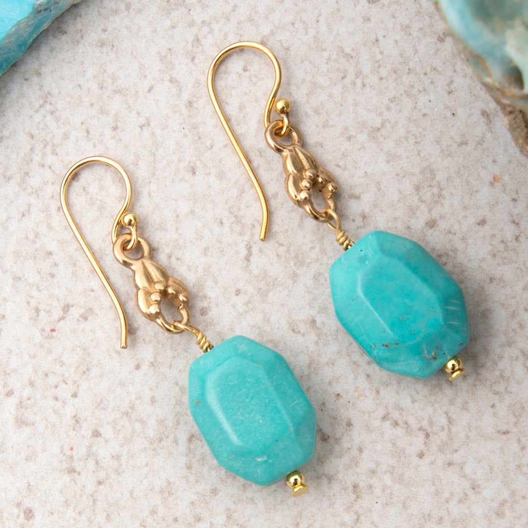 Turquoise earrings with gold hooks on a textured beige surface