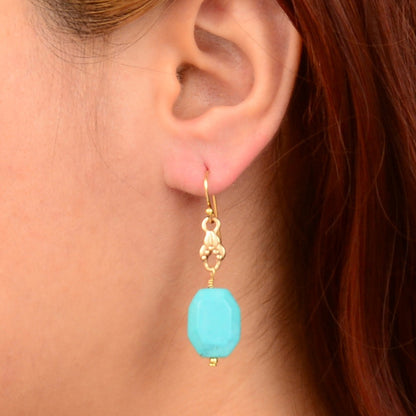 Close-up of an ear wearing a turquoise earring with gold hook.